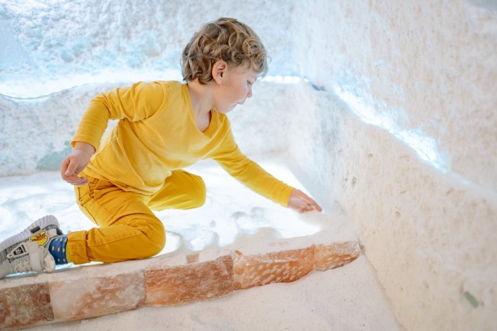 a-boy-playing-on-the-floor-8435770 A young boy in a yellow outfit plays with salt in an illuminated indoor room.