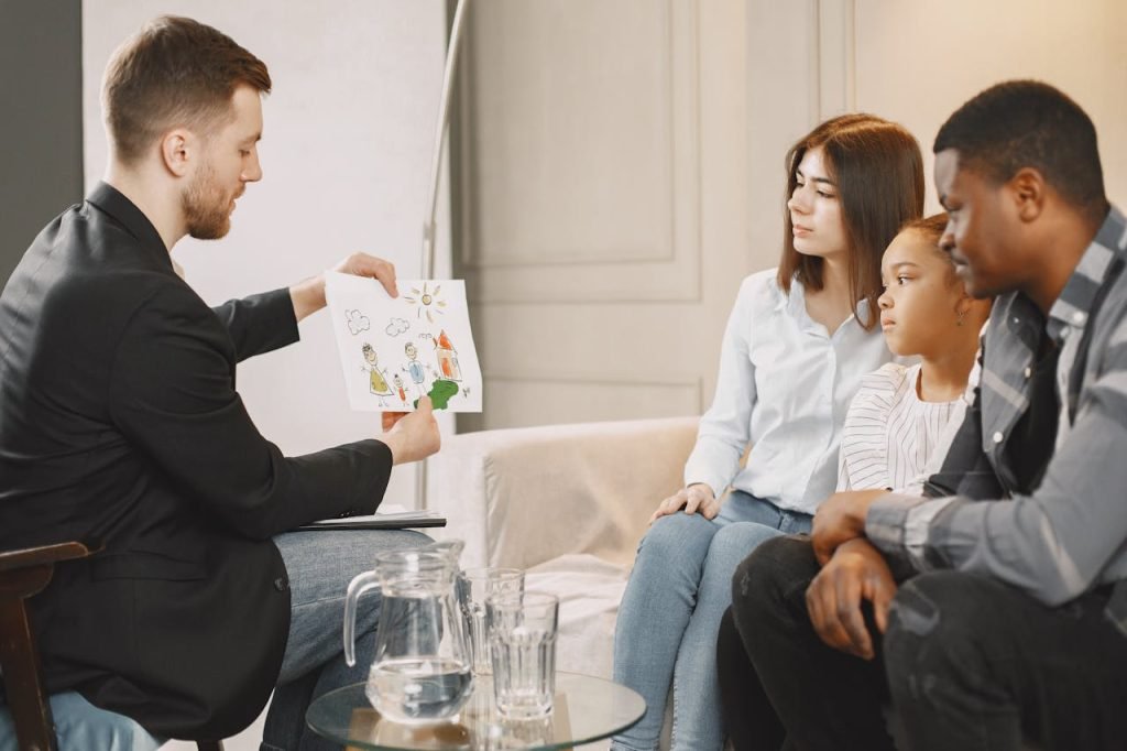 photo-of-a-therapist-showing-a-drawing-to-a-family-7447263 A family therapy session with diverse participants discussing a childs drawing.